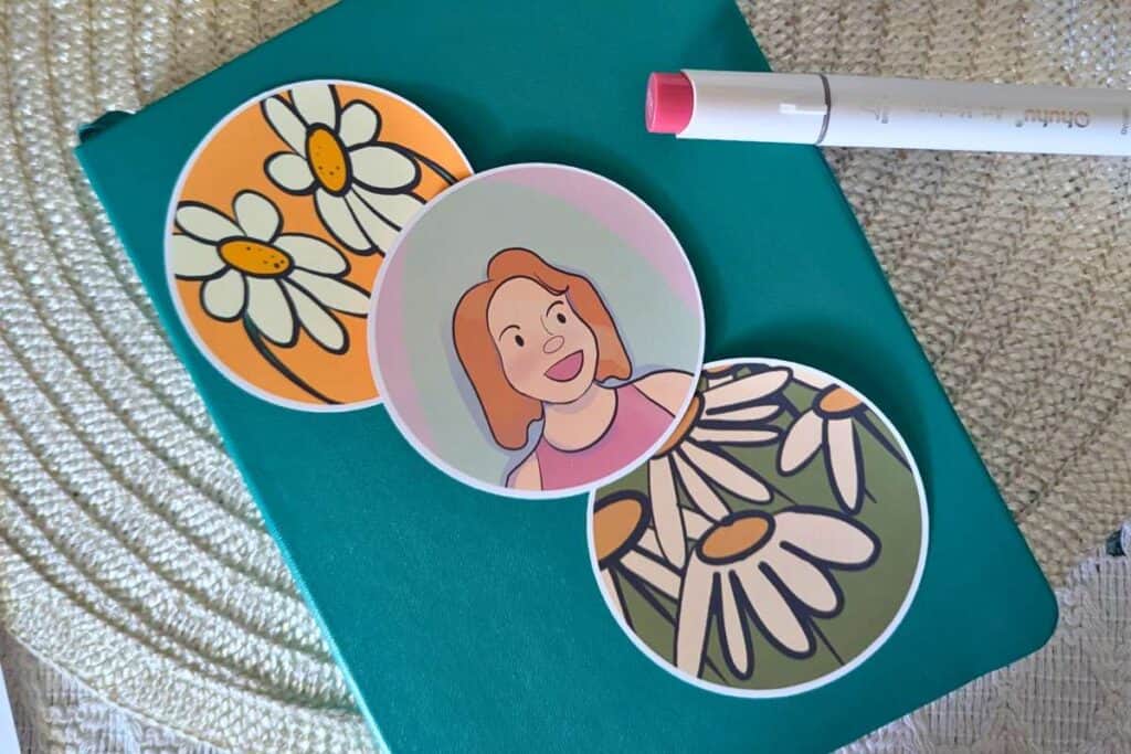 three circle stickers of digital artwork on a teal notebook