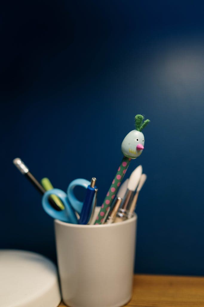 Vibrant office supplies in a white cup against a deep blue background, adding fun to workspace decor.