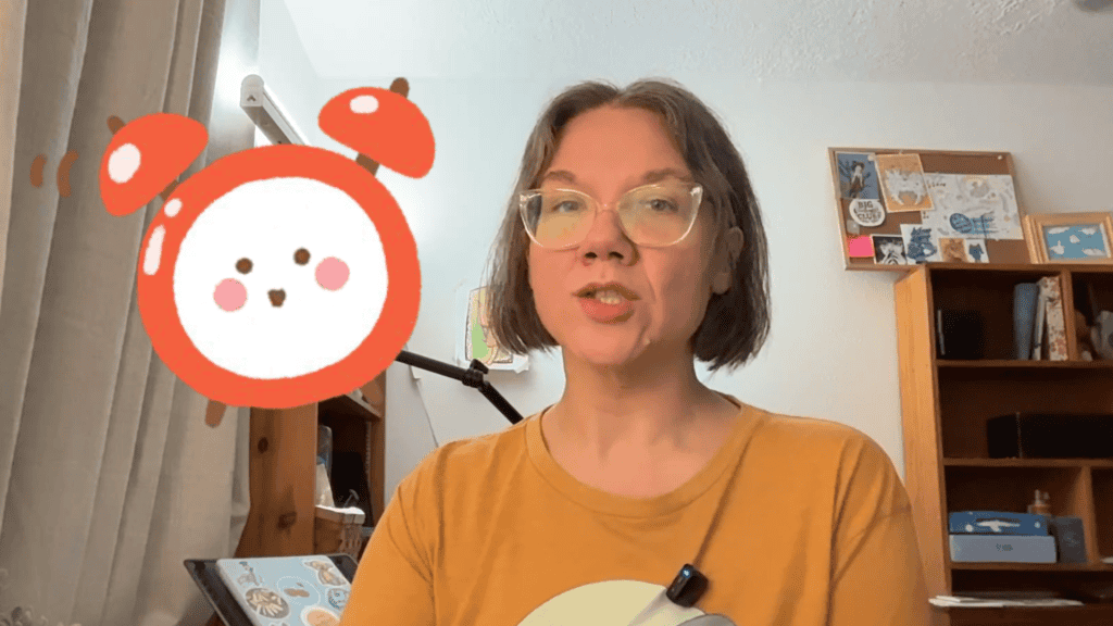 Cynthia McDonald explaining a concept in her art studio with a cute red alarm clock illustration beside her.